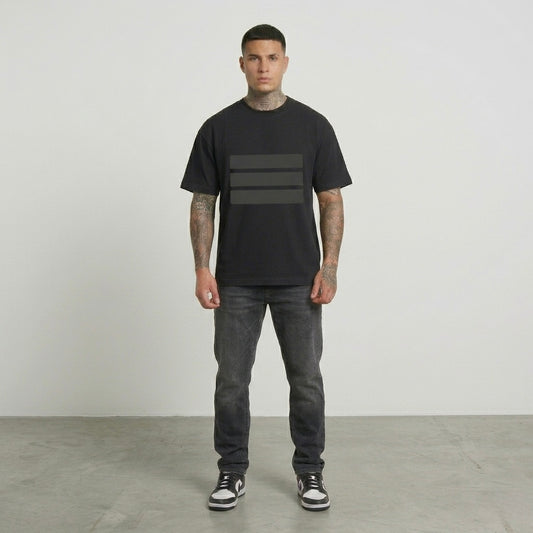 Man wearing a black t-shirt with a graphic design and dark jeans standing against a plain background