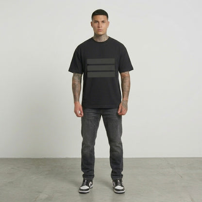 Man wearing a black t-shirt with a graphic design and dark jeans standing against a plain background